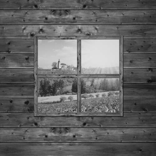 Una finestra in legno di alta qualità, incastonata in una parete di assi di legno, offre una vista su un sereno paesaggio rurale con una chiesa e campi. Questa immagine in bianco e nero simboleggia la personalizzazione e l'integrazione armonica dei serramenti e delle chiusure ProBauen in ogni ambiente, valorizzando la bellezza naturale e architettonica. Rappresenta la nostra capacità di creare soluzioni su misura che uniscono estetica, funzionalità e tradizione, perfette per nuove installazioni o per il restauro di portoni e parti in legno esistenti.