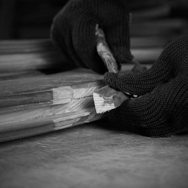 restauro-serramenti-legno-giunzione-artigianato-probauen Primo piano delle mani di un artigiano che, con guanti protettivi, lavora con precisione una giunzione in legno di un serramento. Questa immagine in bianco e nero evidenzia la meticolosa cura e l'artigianalità di ProBauen nel restauro di serramenti e parti in legno, inclusa la riparazione e il rinforzo di giunzioni complesse. Simboleggia la nostra expertise nel ridare nuova vita a infissi e chiusure di alta qualità, garantendo durabilità e integrità strutturale.